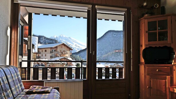 Ein gemütliches Zimmer mit einem Karo-Sofa, einem Holzschrank und einem großen Fenster mit Bergblick.