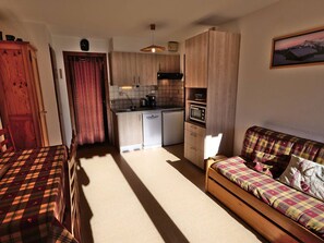 A compact living space with a kitchenette, a dining area with a table and chairs, and a sofa. - Pleasant 2-room + sleeping area, 5 ppl, St Jean de Sixt (Saint-Jean-de-Sixt)