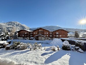 A large wooden building with multiple balconies, surrounded by snow-covered trees and mountains. - Charming studio with alcove - Parking - Praz-sur-Arly (Praz-sur-Arly)