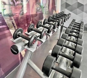A row of black dumbbells on a gym bench with a mirrored wall reflecting a person. - Room-luxury 1-bedroom Stay at Saint Hono (Iloilo)