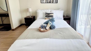 A hotel room with a neatly made bed, a bedside table with a lamp, a window with sheer curtains, and a wall-mounted artwork. - Room-luxury 1-bedroom Stay at Saint Hono (Iloilo)