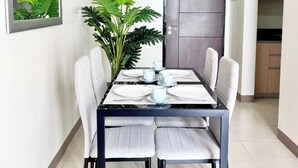 A dining table with four chairs, a potted plant, and a door in the background. - Room-luxury 1-bedroom Stay at Saint Hono (Iloilo)