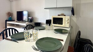 Ett kompakt kök med mikrovågsugn, en liten TV och ett matbord med plats för två personer.