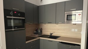 Een kleine keuken met een inbouwoven, magnetron en een gootsteen met een moderne kraan.