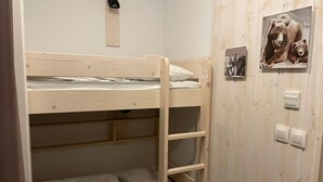Een slaapkamer met een stapelbed, een houten ladder, een klein plankje en een wandlamp.
