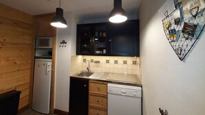 Una cucina compatta con pareti in legno, un forno a microonde, un lavello e una lavastoviglie. Sono presenti due luci a sospensione e un elemento decorativo a parete.