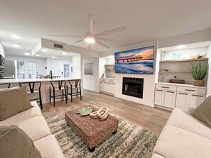A modern living room with a fireplace, a dining area, and a kitchen. - Anastasia Oaks 104B Lo Tide (St. Augustine)