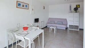 Une petite pièce propre, avec une table blanche dressée pour deux personnes, un canapé et un meuble blanc avec des étagères.
