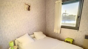 Une chambre à coucher avec un lit, une fenêtre donnant sur un beau paysage, un petit tabouret et un tableau accroché au mur.