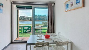 Un coin repas avec une table dressée pour deux personnes, une vue sur un lac et un tableau encadré au mur.