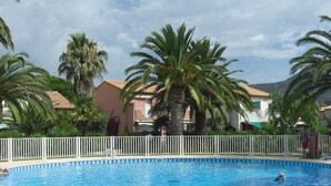 A swimming pool surrounded by palm trees and a white fence, with buildings in the background. - Air-conditioned duplex 2-bedroom with pool and parking - Le Lavandou (Le Lavandou)