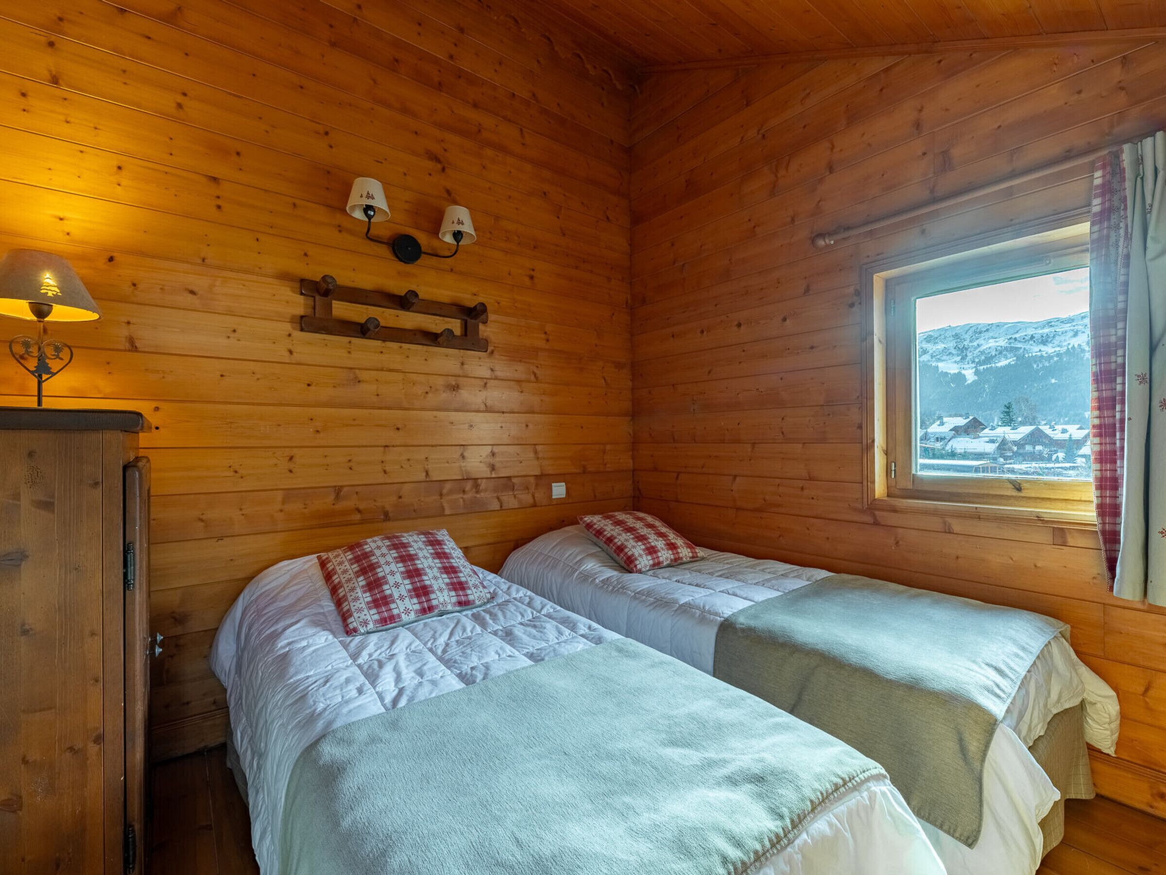 Habitació d'una cabana de fusta amb dos llits, una finestra amb vista a un paisatge nevà i una làmpada penjada a la paret.