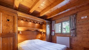 Un dormitorio de cabaña de madera con cama, armario, ventana con cortinas y radiador.