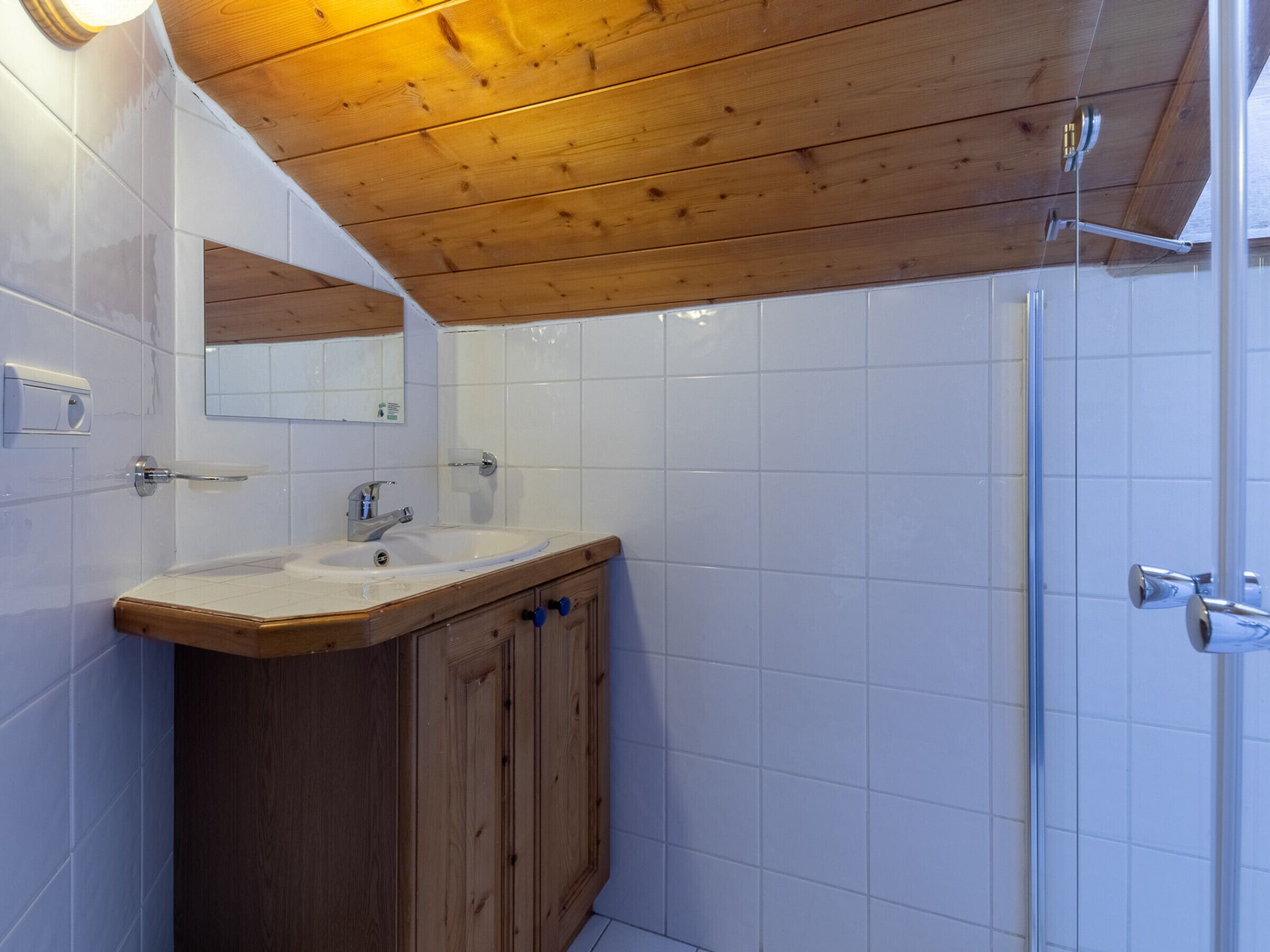 A bathroom with a wooden vanity, a sink, a mirror, and a shower area.