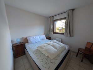 A bedroom with a bed, two bedside tables, a window with curtains, and a chair. - 4 pers. apartment facing slopes with south balcony, near ESF (Montgenèvre)