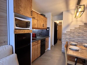 A compact kitchen with wooden cabinets, a built-in microwave, and a black refrigerator. - Cosy and modern apartment for 4/5 people, Falaise area (Avoriaz)