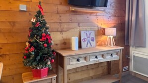 Tunnelmallinen huone, jossa on puuseinä, puisen penkin yläpuolelle asennettu taulutelevisio ja koristeltu joulukuusi.