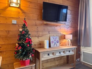 A cozy room with a wooden wall, a flat-screen TV mounted above a wooden bench, and a decorated Christmas tree. - Cosy and modern apartment for 4/5 people, Falaise area (Avoriaz)