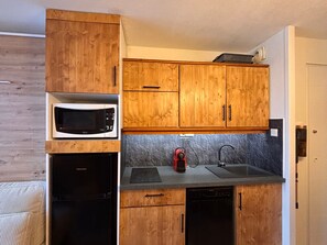 A compact kitchen with wooden cabinets, a microwave, a dishwasher, and a red kettle. - Cosy and modern apartment for 4/5 people, Falaise area (Avoriaz)