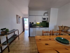 A compact kitchen with white cabinets, a microwave, and a sink. There is a wooden dining table with chairs and a potted plant on the side. - Studio in L'Escala 300m from beach, pool view (L'Escala)