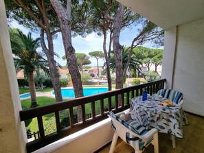Uma varanda com mesa e cadeiras, com vista para uma piscina e árvores.