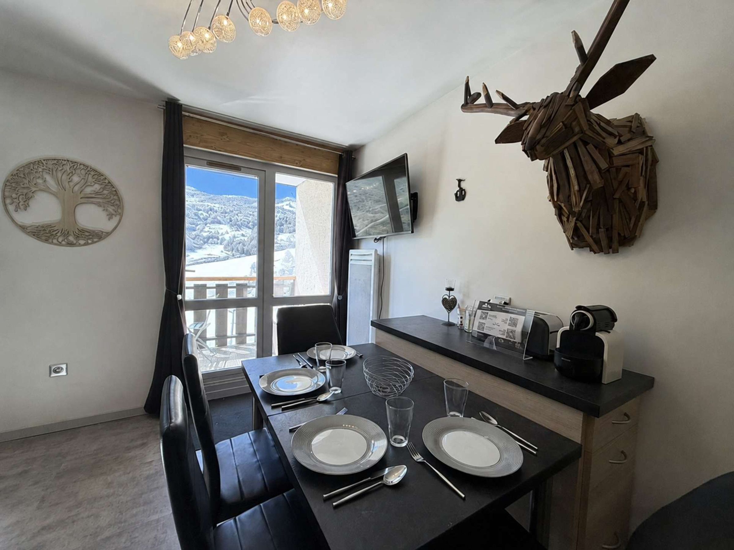 A dining area with a table set for four, a mounted television, and a decorative antler piece on the wall.