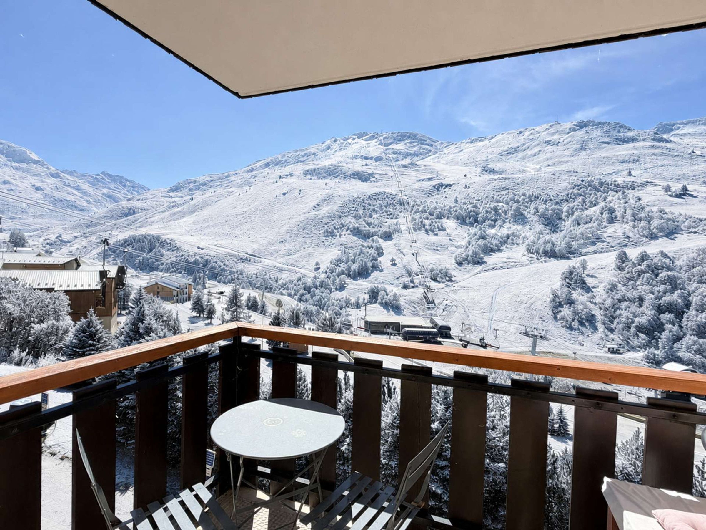 Un balcon avec une table et des chaises, donnant sur un paysage montagneux enneigé.