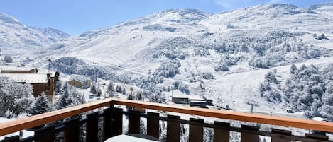 Un balcon avec une table et des chaises, donnant sur un paysage montagneux enneigé.
