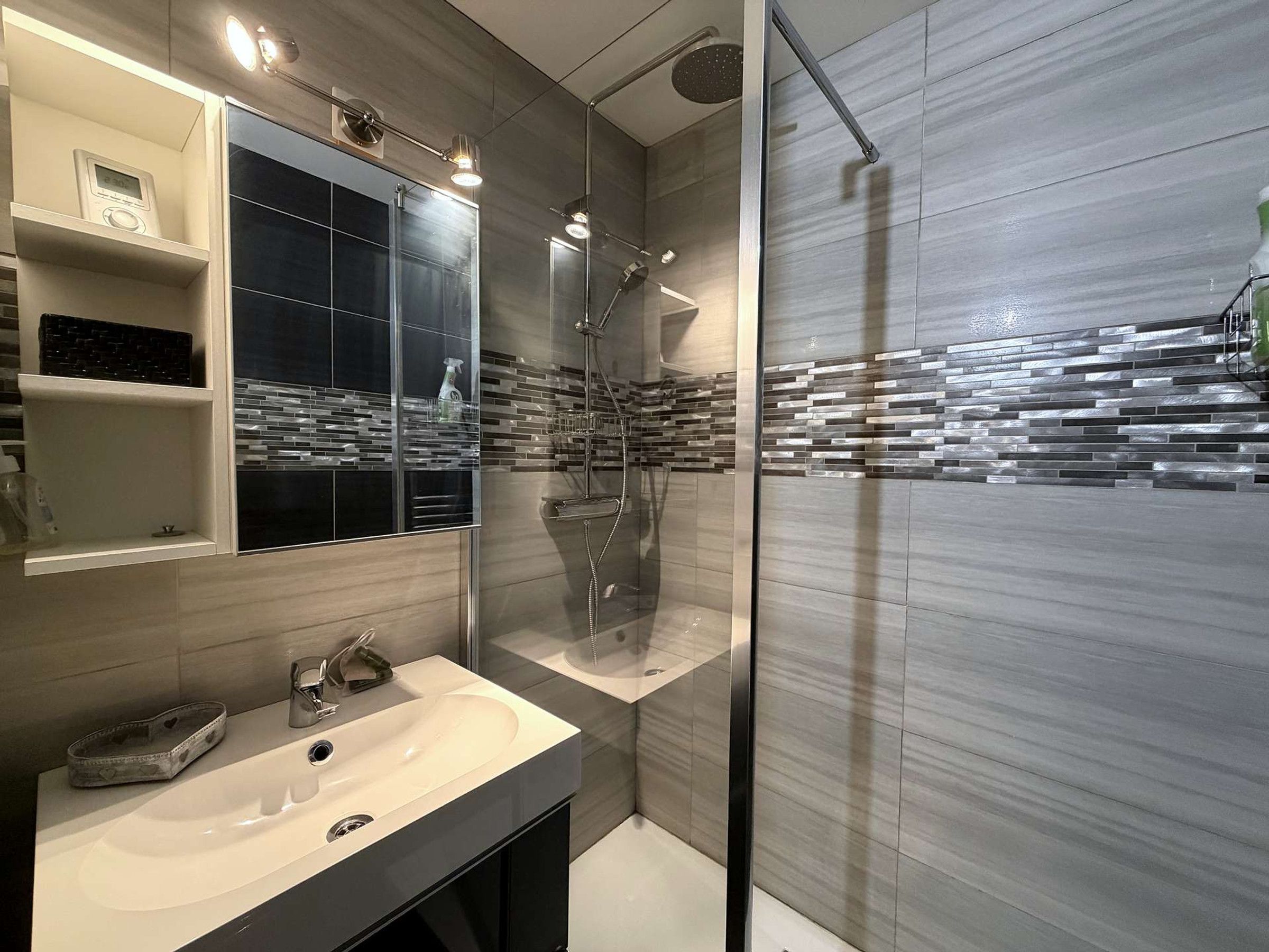 A modern bathroom with a large mirror, a sink, and a shower.
