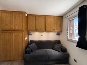 Ein Zimmer mit einem dunkelgrauen Sofa, Holzsäcken und einem Fenster mit Blick auf schneebedeckte Berge.