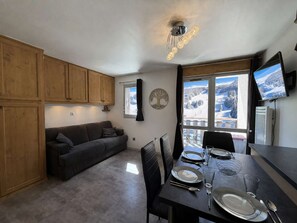 Eine moderne Küche mit Holzausstattung, einem Esstisch für vier Personen und einem großen Fenster mit Blick auf verschneite Berge.
