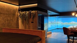 A modern bedroom with a large bed, a wooden headboard, a glass wall, and a dining area with a table and chairs. - Immerse yourself in 20 natural settings around your infinity pool and jacuzzi. (Lasne)