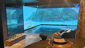 A modern dining area with a panoramic aquarium view, a wooden dining table set with plates, glasses, and cutlery, and a comfortable seating arrangement. - Immerse yourself in 20 natural settings around your infinity pool and jacuzzi. (Lasne)