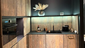 A modern kitchen with wooden cabinetry, a black countertop, and a backsplash. There is a vase with dried pampas grass, a wine bottle, and a coffee machine on the counter. - Immerse yourself in 20 natural settings around your infinity pool and jacuzzi. (Lasne)