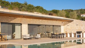 Uma área moderna de piscina ao ar livre, com paredes de pedra, um deck de madeira e espaço para refeições.