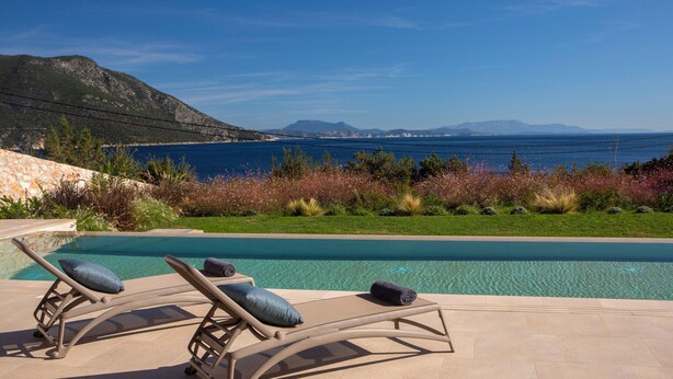 Área de piscina com espreguiçadeiras e vista para o mar e montanhas.