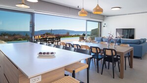 Uma cozinha moderna com uma ilha grande, área de refeições com cadeiras e vista para o mar.