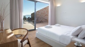 Quarto de hotel moderno com uma cama grande, uma escrivaninha, uma cadeira e vista para o mar através de uma porta de vidro deslizante.