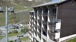 Um edifício com várias andares e varandas, um teleférico ao fundo, e uma paisagem montanhosa.