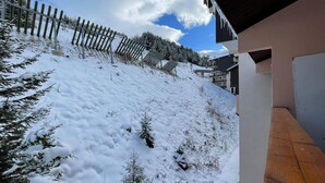 Encosta coberta de neve, com cerca de madeira e um edifício com telhado inclinado.