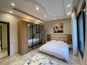 A modern bedroom with a large bed, a wardrobe, a mirror, and a painting on the wall. - Spacious -2 bedroom apartment in adorable El Shikh Zaid with AC (El Shikh Zaid,)