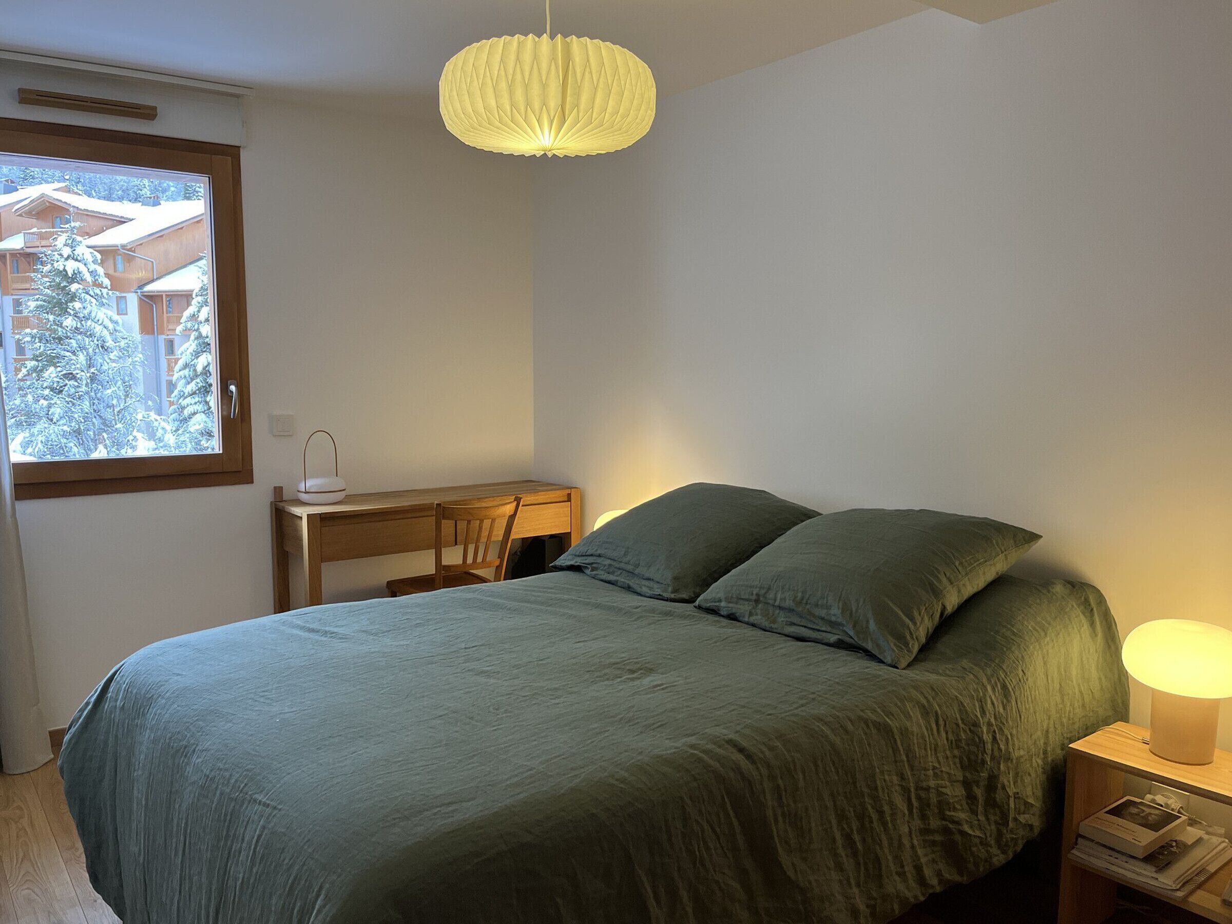 Un dormitorio con una cama, un escritorio, una silla, un ventanal y una lámpara colgante.