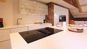 Eine moderne Küche mit weißen Schränken, einer schwarzen Induktionskochplatte und einer Holzbalkendecke.