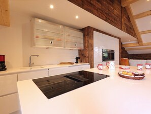 A modern kitchen with white cabinetry, a black induction cooktop, and a wooden ceiling.