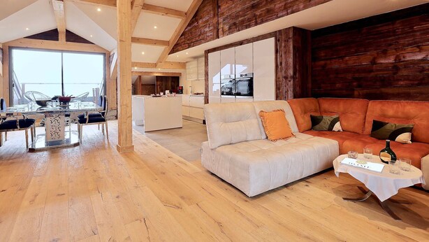 Ein großzügiger Wohnbereich mit hohen Decken, Holzbalken, einem großen Sofa und einer Essecke mit einem Glastisch.