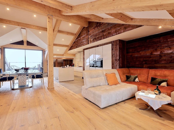 A spacious living area with a high ceiling, wooden beams, a large sofa, and a dining area with a glass table.