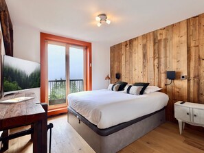 Ein Schlafzimmer mit einem großen Bett, einer Holzwand, einem Fernseher und einem Balkon.