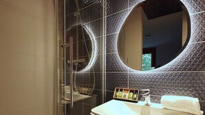 Ein modernes Badezimmer mit Duschkabine aus Glas, einem runden Spiegel und einem Waschtisch mit Pflegeprodukten.