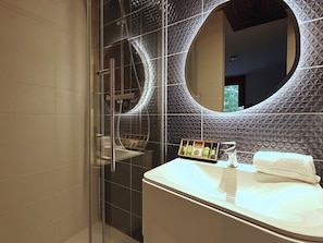 A modern bathroom with a glass shower enclosure, a round mirror, and a vanity with toiletries.
