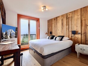 A bedroom with a bed, a desk, a TV, and a wooden wall.